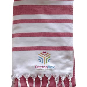 A striped Turkish beach towel in red and white, featuring tassels and a logo at the bottom.