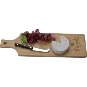 A bamboo serving board with a cheese round, grapes, and a cheese knife, featuring a logo on the surface.