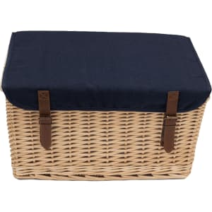A wicker picnic basket with a navy blue fabric lid and brown leather straps, featuring a logo on the front.