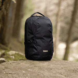 A black laptop backpack with a side pocket and a logo, set against a natural outdoor background.