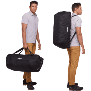 A duffel bag in black with a mid blue accent, featuring a shoulder strap and handles, held by a person.