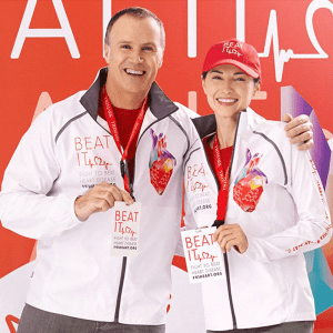 Two individuals wearing white Egmont Packable Jackets with a logo, posing with medals and a red hat.