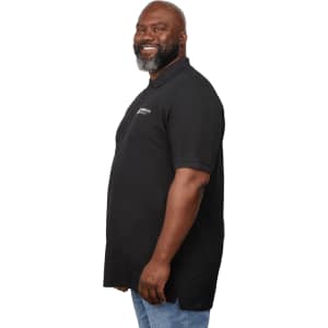 A man in a black polo shirt with a logo, standing with a smile and facing left. The shirt has a longer cut.