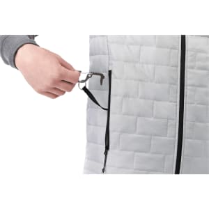 A hand pulls a key clip from a zip pocket on a grey insulated puffer vest. The vest features a quilted design.
