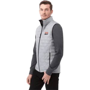 A lightweight, packable insulated puffer vest in light grey, featuring a logo, worn over a long-sleeve grey top.