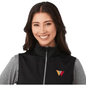 A black softshell vest featuring a zippered front and a logo. The model wears a grey long-sleeve top underneath.