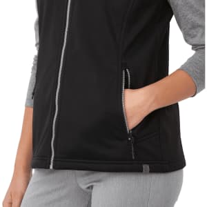 A black women's softshell vest featuring a zip front and side pockets, with grey sleeves and a branding logo.