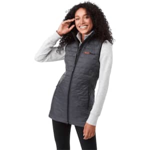 A woman wearing a grey insulated puffer vest over a light grey long-sleeve top, smiling while posing.