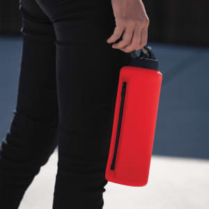 A drink bottle in vibrant red with a black zippered section, held by a person wearing black pants.