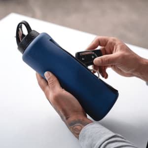 A drink bottle in navy blue with a zippered compartment, held by a person with tattoos.