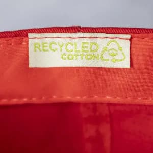 A tag for a product made from recycled cotton, featuring a bright red fabric background.