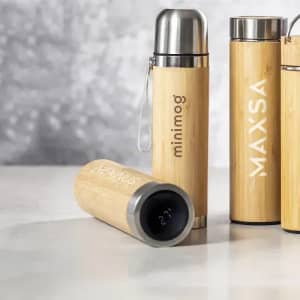 A drink bottle made of bamboo with a stainless steel cap and a logo, placed on a textured surface.