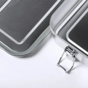 A lunchbox with a silver metallic finish, featuring a hinged lid and metal clasp for secure closure.
