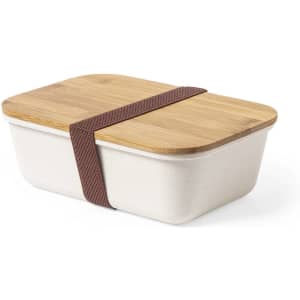 A lunch box featuring a beige container and a bamboo lid, secured with a brown elastic strap.
