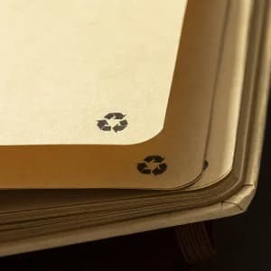 A stack of brown notebooks featuring recycled paper with black recycling symbols on the corners.