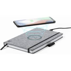 A notebook with a grey fabric cover, featuring a wireless charging circle, beside a smartphone.