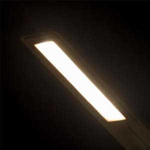 A light fixture emits a warm white glow, featuring a sleek, rectangular design. It has a modern aesthetic and is mounted on a dark surface.