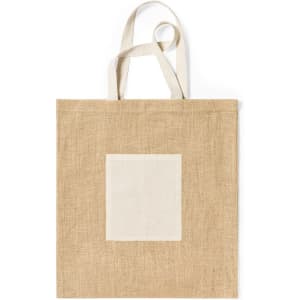 A jute tote bag in a natural beige colour with a plain cream square patch on the front. Features matching fabric handles.