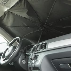 A black umbrella positioned inside a car, covering the windshield. The steering wheel and dashboard are visible.
