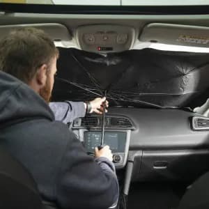 A man using an umbrella to shield the dashboard of a car. The umbrella is black and is opened inside the vehicle.