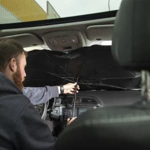 A person inside a car is using an umbrella to block sunlight, with a broken canopy visible.