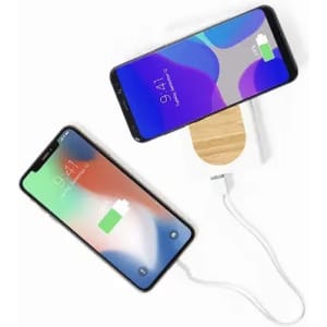 A wireless charger with a wooden base and two smartphones, one displaying a battery charging icon.