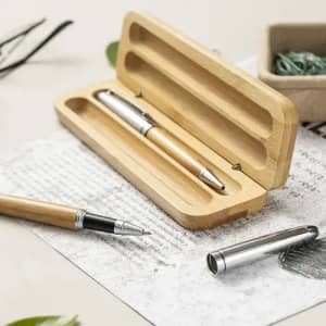 A wooden pen set with a bamboo case and a silver pen, placed on textured paper with greenery in the background.
