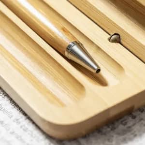 A wooden pen with a silver tip resting in a bamboo holder, surrounded by a light wooden surface.
