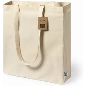 A tan fairtrade tote bag with long handles, featuring a tag and a small logo on the side.