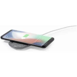 A wireless charger in grey with a smartphone resting on it, displaying a charging icon on the screen.