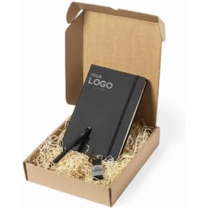 A gift box featuring a black notebook, pen, and a keychain, all set in shredded paper. The box has a logo on it.