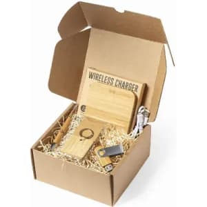 A gift box featuring a wooden wireless charger, USB drive, keyring, and earphones, all on a bed of straw.