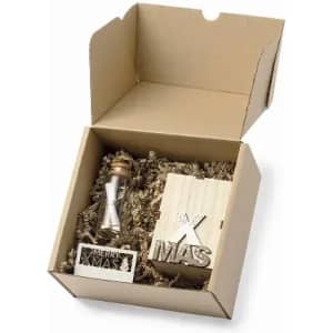 A gift box containing a small hourglass and wooden decorations, nestled in shredded paper. The box is open.