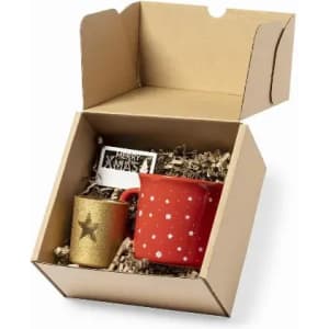 A gift box containing a red mug with stars and a gold cup with a star, filled with decorative filler.