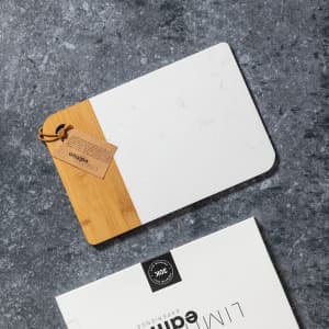 A rectangular chopping board featuring a bamboo edge and a matte white surface, with a tag attached.
