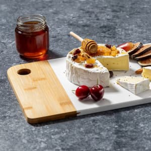 A cheese board featuring a wheel of brie, honey jar, cherries, and assorted crackers on a grey surface.