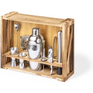 A wooden crate display containing a cocktail shaker, jigger, strainer, spoon, and other bar tools in metallic finishes.