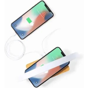 A wireless charging pad in a natural wood finish, powering two smartphones with white cables.