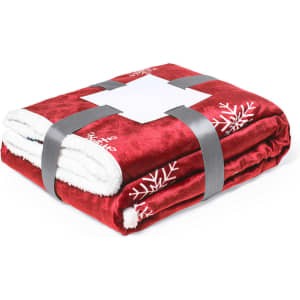 A red fleece blanket with white snowflake designs, neatly folded and secured with a grey ribbon.