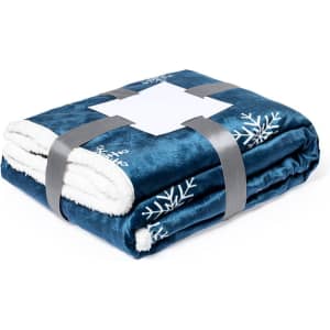 A plush navy blue blanket folded with a soft white underside, decorated with snowflake patterns, secured with a grey strap.