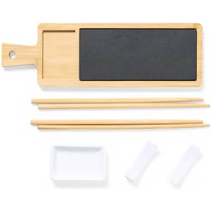 A bamboo serving board with a black slate section, two sets of chopsticks, a small white dish, and two sauce holders.