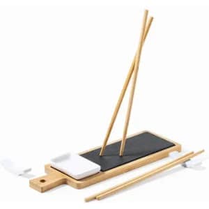 A bamboo chopstick holder set featuring a black slate surface, white dipping dish, and bamboo chopsticks.