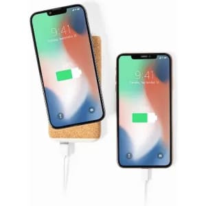 A wireless charger with two smartphones displaying charging indicators. The charger has a natural cork surface.