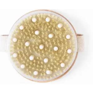 A round body brush with a textured golden bristle surface and small white beads, featuring a fabric strap.