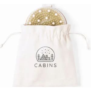 A round brush with a textured surface and white pearls, stored in a drawstring cotton bag featuring a simple logo.
