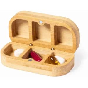 A bamboo pill organiser with three compartments and a small red, yellow, and white capsule inside. It has a logo.