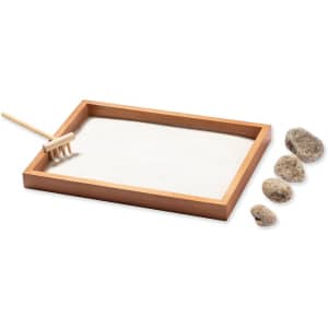 A sand tray with a wooden frame, a small rake, and several smooth stones in the foreground.