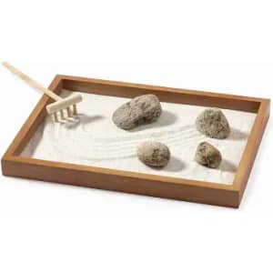 A mini sand garden featuring a wooden tray filled with white sand, smooth rocks, and a small rake.