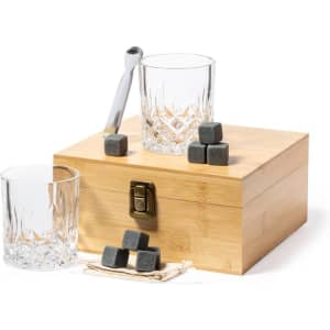 A wooden box with a clasp holds grey ice cubes beside two crystal glasses and a metal spoon.