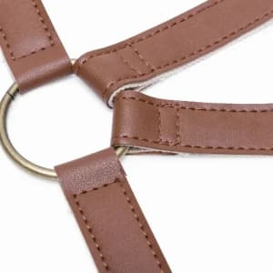 A brown leather harness with a circular metal ring at the centre, featuring adjustable straps.